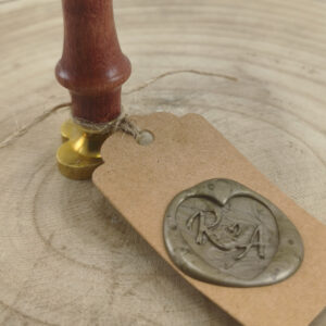 Close-up of a wooden stamp with a gold base resting on a kraft tag tied with twine, on a wooden surface.