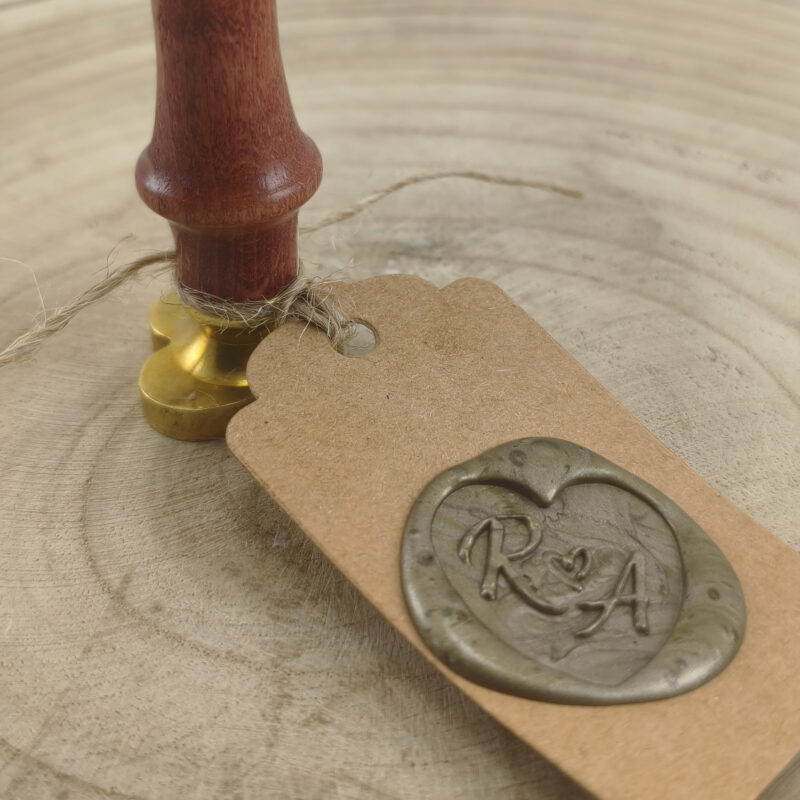 Close up of a Wooden Stamp with a Gold Base Resting on a Kraft Tag Tied with Twine on a Wooden Surface
