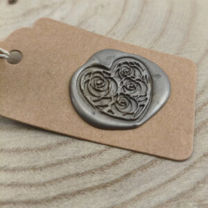 Brown kraft tag with a dark gray heart-shaped wax seal featuring rose motifs.